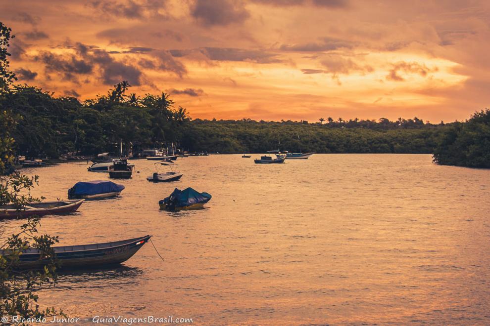 Imagem de um lindo entardecer e barcos no rio em Caraiva.